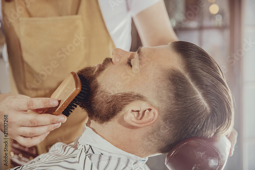 The barber combs the man's beard with a brush. Photo in vintage style