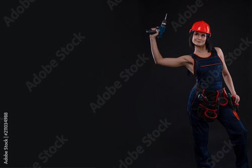 Attractive young woman doing repairs at black background. Portrait of a female construction worker. Building, repair concept. Copy space