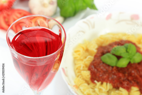 Lampka czerwonego wina i makaron spagetti z sosem neapolitańskim.