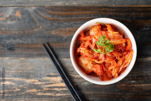 Kimchi cabbage in a bowl with chopsticks for eating on wooden background, top view, Korean food