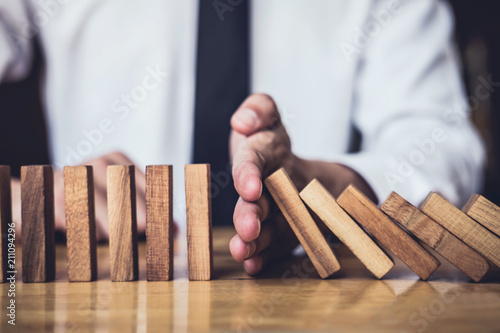 Strategy and successful intervention concept for business, businessman hand Stopping Falling wooden Dominoes effect from continuous toppled or risk