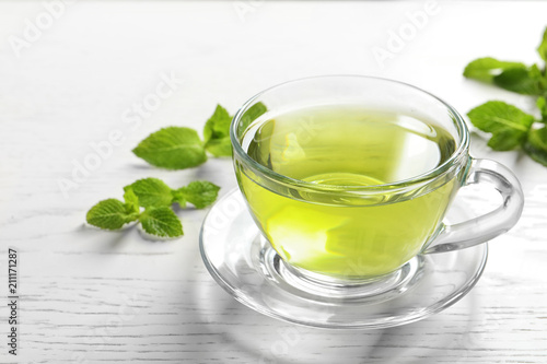 Cup with hot aromatic mint tea and fresh leaves on table