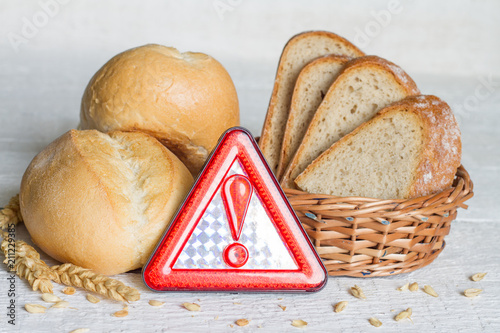 Gluten intolerance with bread wheat and warning sign on white planks 