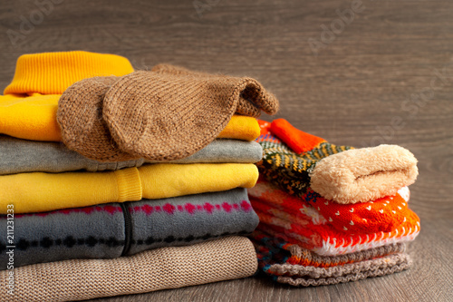 A stack of warm clothes on a wooden background. Colorful warm clothes. Knitted sweatshirts and sweaters, knitted socks, orange mittens for autumn and winter cold seasons.