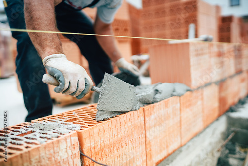 Professional worker using pan knife for building brick walls with cement and mortar