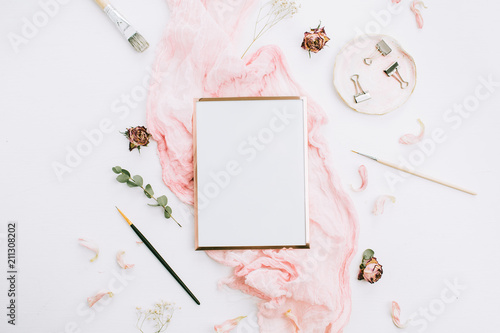 Creative festive composition with photo frame mock up, pink blanket, flowers, eucalyptus branches and brushes on white background. Flat lay, top view stylish template.