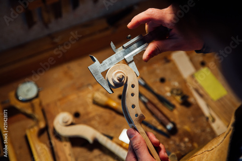 Master artisan luthier working on creation of a violin scroll. detailed work on wood with tools.