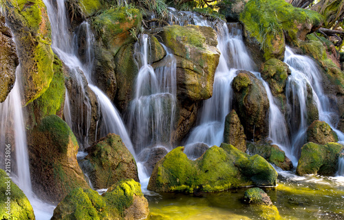 Waterfall, huge boulders are covered with moss. The stones are flooded with sunlight.