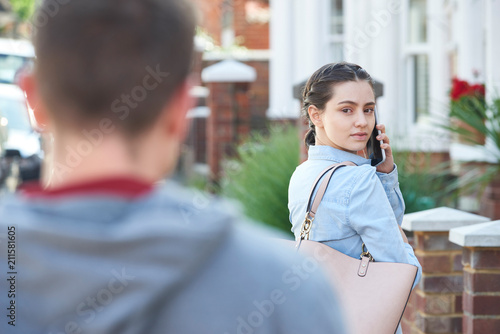 Young Woman Calling For Help On Mobile Phone Whilst Being Stalked On City Street By Man