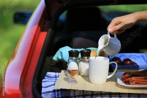 Kobieca ręka nalewa mleko do kubka, piknik w bagażniku samochodu.