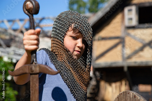 A young boy disguised as an unblemished knight with a sword, shield and basinet. 