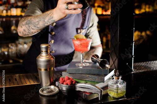 Bartender strewing on the red transperent cocktail standing on the books