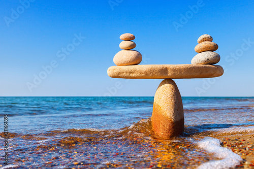 Symbolic scales of the stones, illuminated by the evening sun, against the sea, close-up. Pros and cons concept