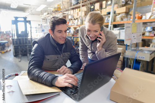 managers working on laptop and talking on phone in warehouse