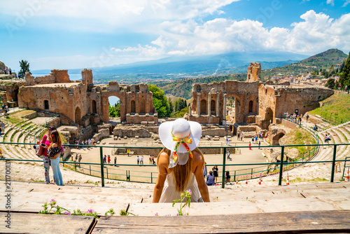 Jule 04, 2018. Taormina, Italy. Beautiful girl in a long white dress and white summer hat sitting at the caldron of the ancient Greek Theater of Taormina in Italy.