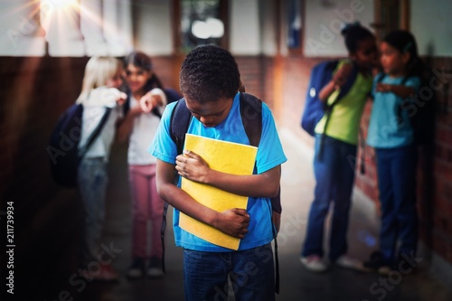 Sad pupil being bullied by classmates at corridor