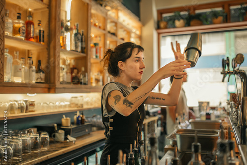 Young female bartender mixing cocktails behind a bar counter