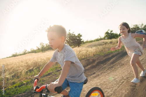 Boy and girl in the field. The boy is riding a bicycle, and the girl is running alongside. A cheerful, happy childhood in the village.