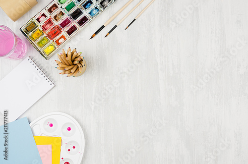 Back to school background - stationery for creativity - watercolor paints, palette, brushes, colored pencils on white wood table, top view.