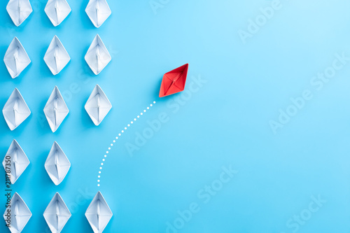 Group of white paper ship in one direction and one red paper ship pointing in different way on blue background. Business for innovative solution concept.