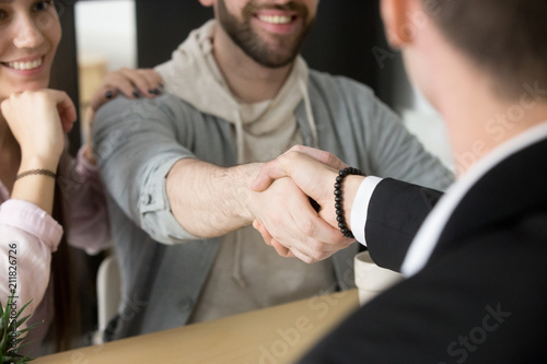 Close up of satisfied couple shaking hand of realtor or broker, closing purchase deal on buying first home together, husband handshaking insurance agent or lawyer thanking for successful negotiations