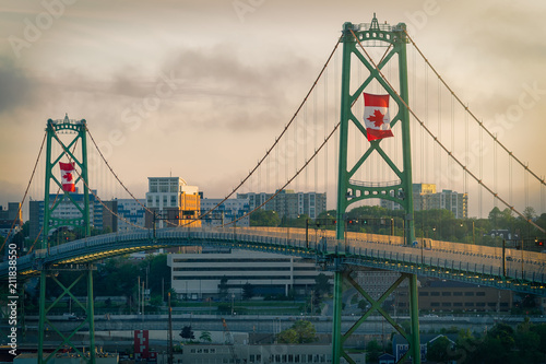 The Angus L MacDonald Bridge at dusk on Canada Day with large Canadian flags flying.