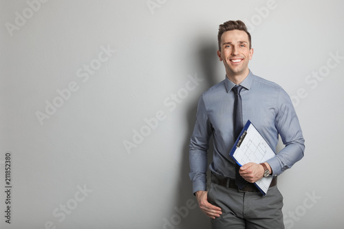 Male real estate agent with clipboard on grey background