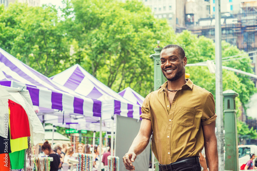 Summer Street Fair and Flea Market in New York. Young African American Man shopping, traveling in New York, wearing green short sleeve shirt, walking by street in Midtown of Manhattan, smiling..