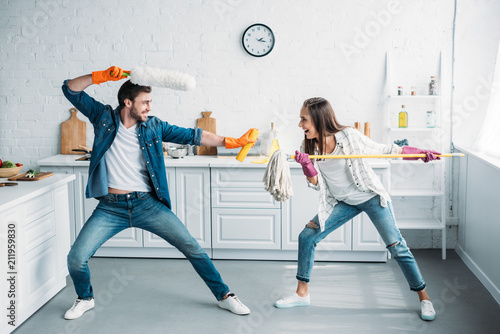 couple having fun and pretending fight with cleaning tools in kitchen