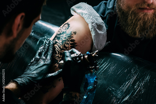 cropped shot of tattoo artist in gloves working on tattoo on shoulder in salon