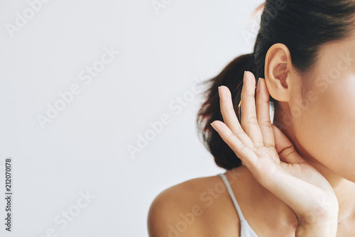 Crop female with dark hair in ponytail touching ear with help of fingers and with tenderness on grey background