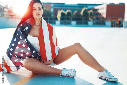 Sexy woman covered by USA flag sitting outdoors in sunlight