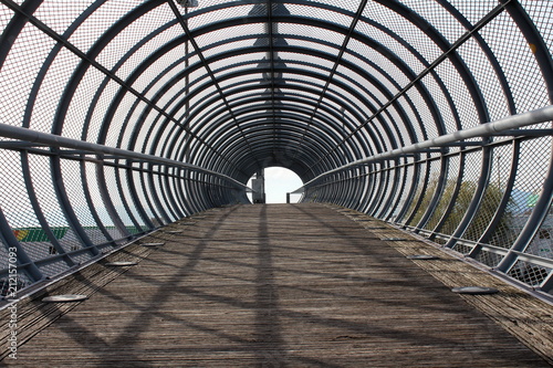 Strong metal bars bridge in shape of tunnel with wooden walkway and round floor lights on both sides