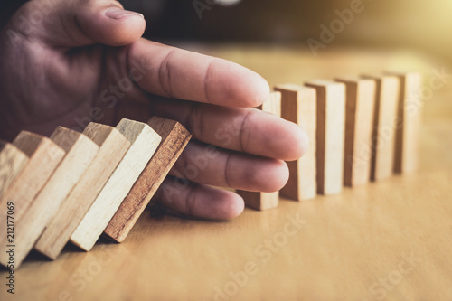 Strategy and successful intervention concept for business, businessman hand Stopping Falling wooden Dominoes effect from continuous toppled or risk