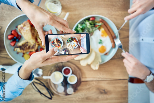 Woman taking photo of breakfast served in cafe. Couple having meal together