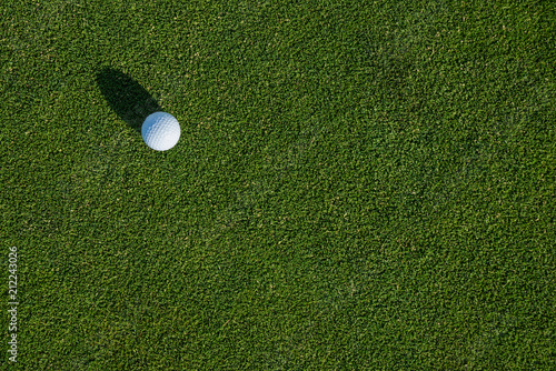 Early morning on the golf green, still covered in dew and sparkles from the sun, side light on a golf ball and a big shadow 