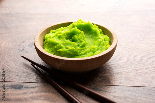 Green wasabi sauce or paste in bowl, with chopsticks or spoon over plain colourful background. selective focus