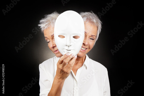 older woman hiding happy and sad face behind mask, concept for manic depression or bipolar or dramedy comedy drama