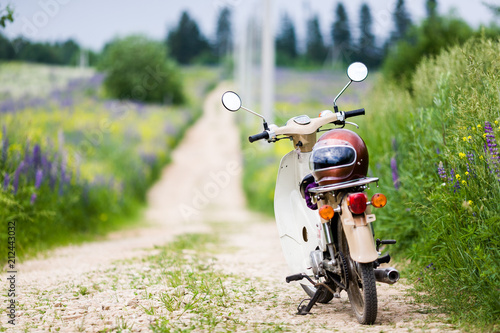 Classic old light motor retro moped with an old school helmet on a country road among green fields on a warm summer day