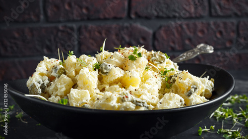Warm potato salad with gherkins in a black plate
