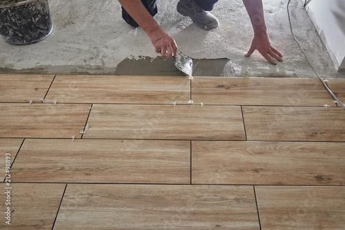 Hands of the tiler are laying the ceramic wood effect tiles on the floor