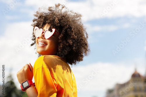 Beaming with pleasure. The portrait of a cheerful young woman in heart-shaped sunglasses posing for the camera in the city center