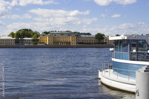 View of the historic building of the Menshikov Palace built in 1714 and the University embankment on the opposite bank of the broad Neva River at the pier on a summer sunny day in St. Petersburg in Ru