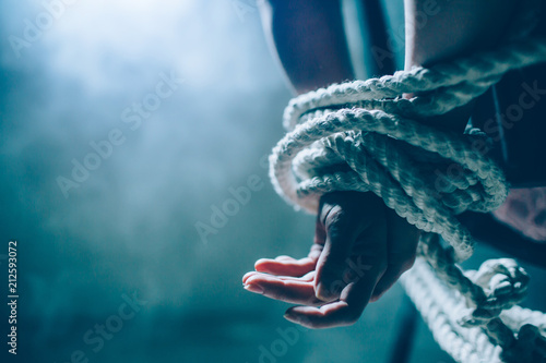 Close up and cut view of woman's hands died in a knot with a rope. One hand is up on another. Woman is tied behind her back. There is a window in dark room. Also there is a white smoke..