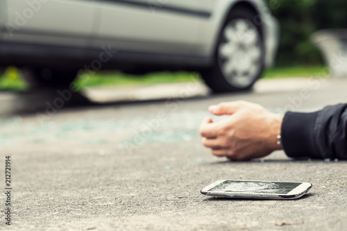 Broken phone next to a hand of a victim lying on the street