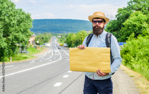 Short general directions. Man bearded hitchhiker stand at edge of road with blank paper sign, copy space. Benefits using sign with name destination. Cardboard sign with indication where you want go