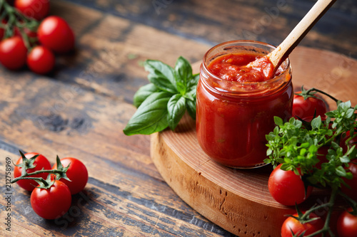 Tomato sauce in a glass jar, tomatoes and herbs on its side.