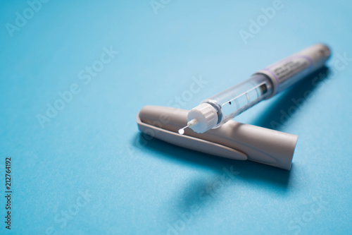 Insulin pen with insulin drop at needle tip on light blue background. Medical devices is used to self-injection for treatment diabetes disease and control blood sugar. World diabetes day. Copy space.