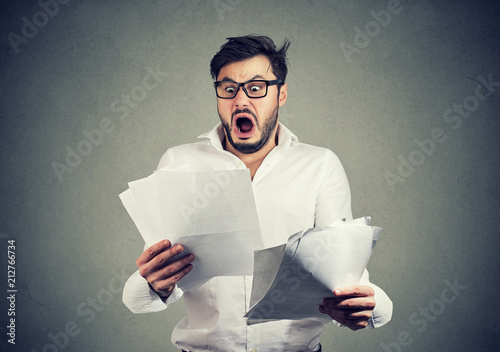 Shocked business man looking through papers with bills