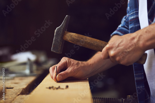 Carpenter hammering a nail into wooden plank in a carpentry shop